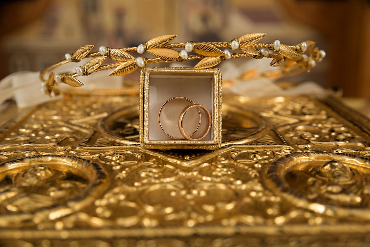 gallery-6 Close-up of gold wedding rings and a delicate tiara on an ornate golden background, symbolizing luxury and elegance.
