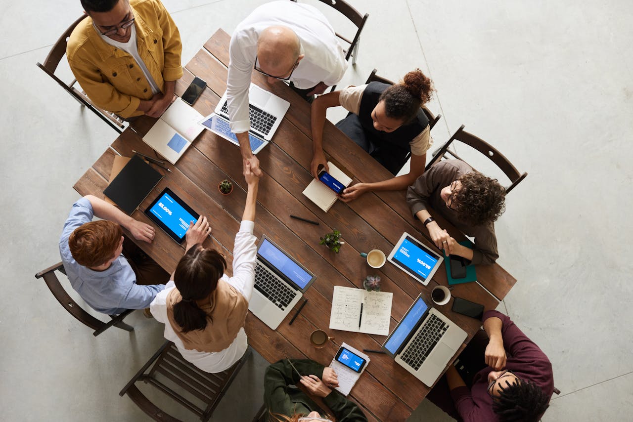 about-img Top view of a diverse team collaborating in an office setting with laptops and tablets, promoting cooperation.