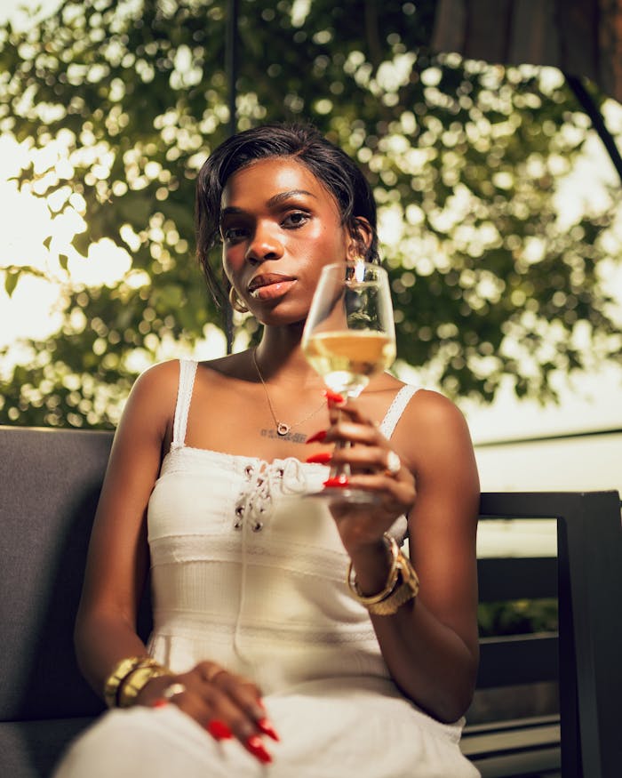 gallery-2 Sophisticated woman in white dress holding a wine glass outdoors, creating a serene and luxurious vibe.