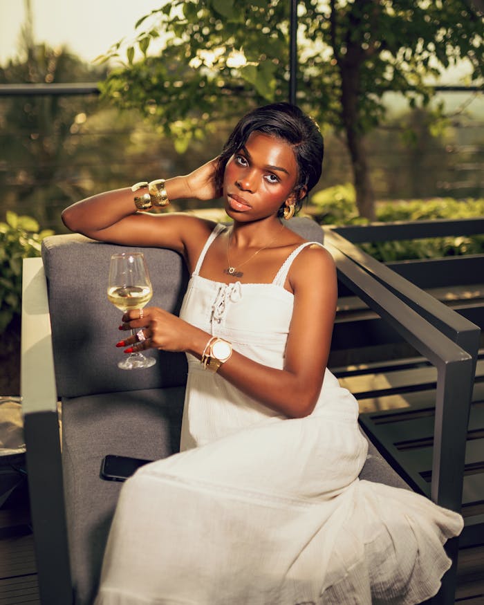 why-choose-us Elegant woman in white dress enjoying a glass of wine outdoors on a sunny day.